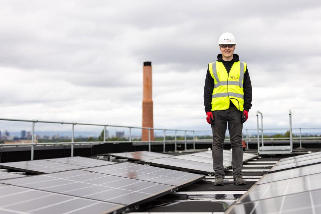 An engineer in a hard hat and safety vest inspects solar panels on a rooftop.